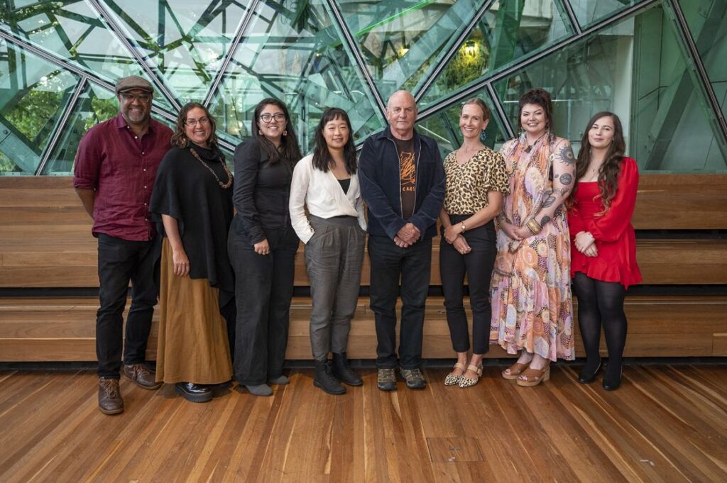 eight people standing in a row, smiling at the camera