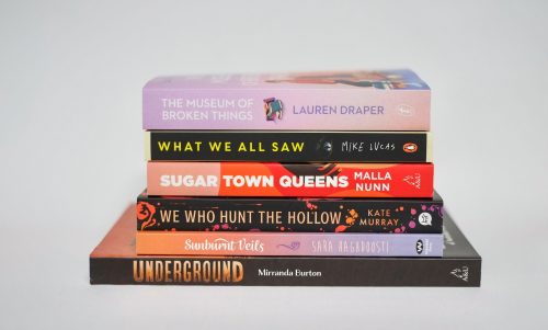 A stack of books: Museum of Broken Things; What We All Saw; Sugar Town Queens; We Who Hunt The Hollow; Sunburnt Veils; and Underground