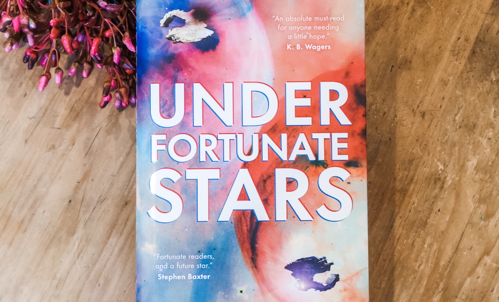 Under Fortunate Stars book sitting on wooden table with red flowers